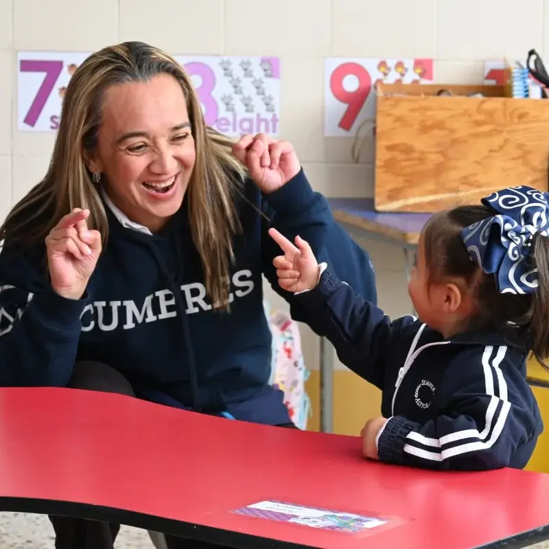 Maestra interactúa con alumna en aula colorida durante actividad educativa en Instituto Cumbres.